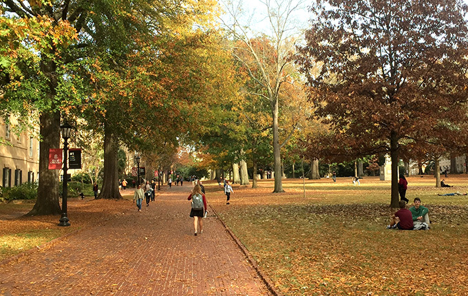 Students walking the brick walkways of the USC Horseshoe, surrounded by trees and historic buildings.