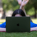 girl laying down in green grass and looking at laptop