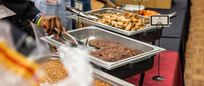 A person uses tongs to pick up food in a buffet line