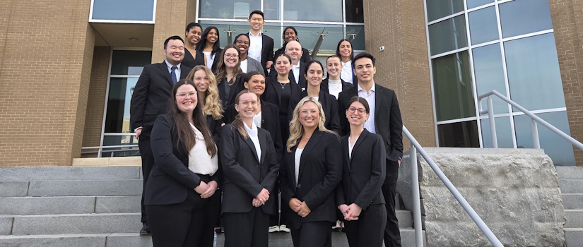 Group of 19 professionally dressed individuals posing on outdoor steps in front of a modern brick and glass building.