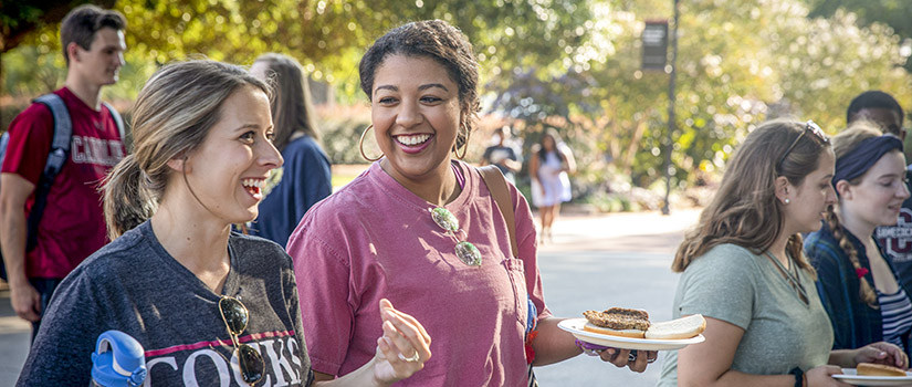 Several students smiling on Greene Street with food on their plates.