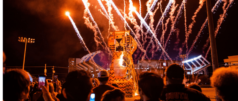 Student watching a tiger created by engineering students burn in front of Williams Brice Stadium. Fireworks going off in the background.