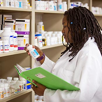 Pharmacy student standing in front of a shelf of medication reading a lable from a medicine bottle.