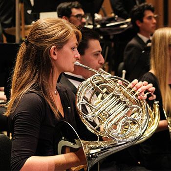 Student playing a french horn at a music ensemble concert.
