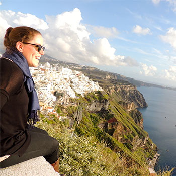 Student sitting on a cliff overlooking a city and water.
