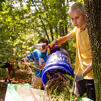 Student collecting sticks and trash at a park.