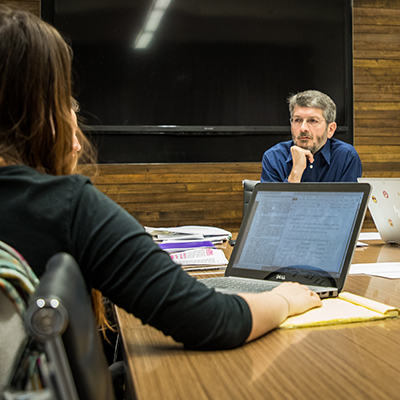 Professor sitting at a table having a discussion with students.