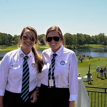 Students in a uniform standing on a balcony overlooking a golf course.