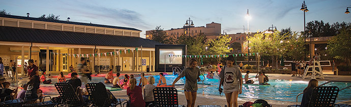 The outdoor pool at the fitness center at dusk with people hanging out getting ready to watch a movie at the Dive-In Movie event.