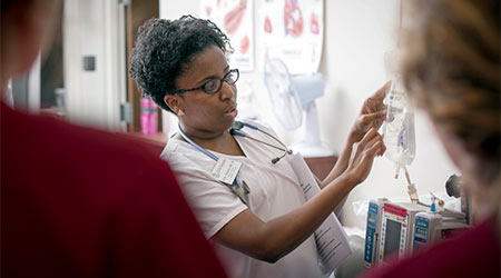 A nursing professor holding an IV bag instructing students in garnet scrubs.