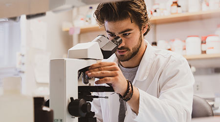 A student looking into a microscope wearing a lab coat.