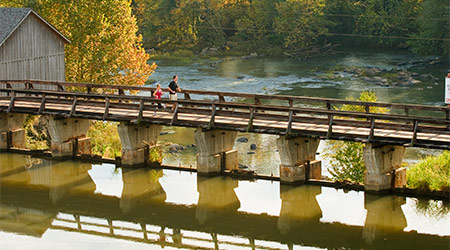 Two people walking on the bridge across the canal at the river.