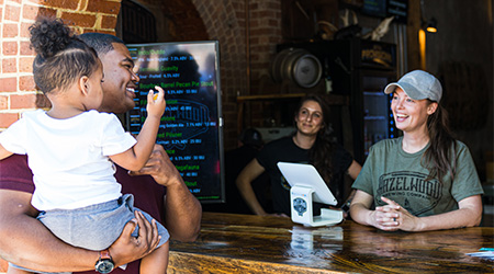 A dad holds a little girl while ordering at an outdoor restaurant.