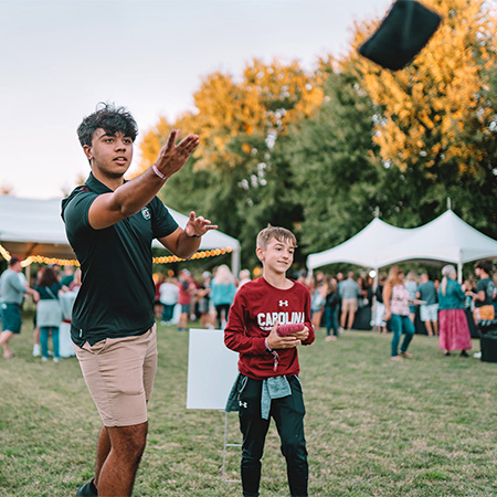 Student and a younger kid playing corn hole.