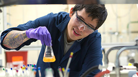 Student at a lab bench swirling a yellow liquid in a beaker.