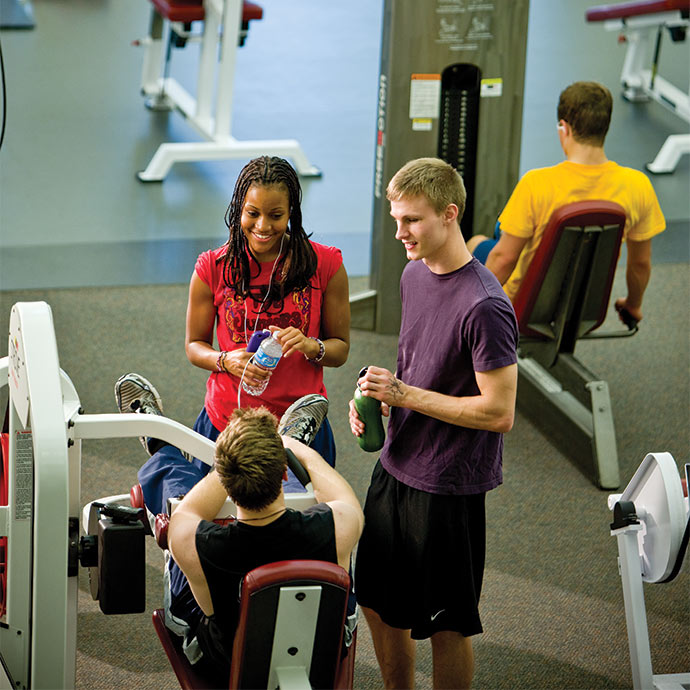 Three students gathered at a weight bench drinking water.