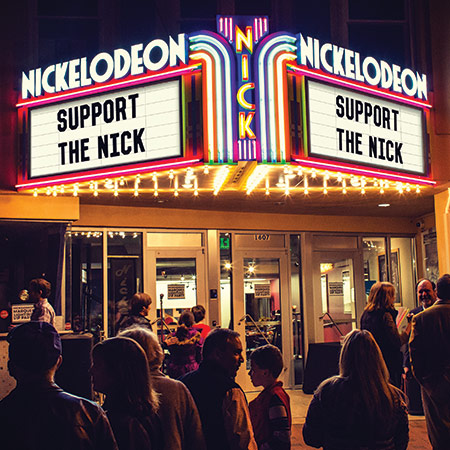 Glowing marque from the Nickelodeon theater with the text Nickelodeon Support the Nick on it and people gathered around out front.