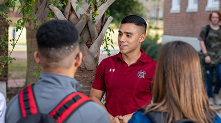 Student ambassador giving a tour outside with a palmetto tree behind him.