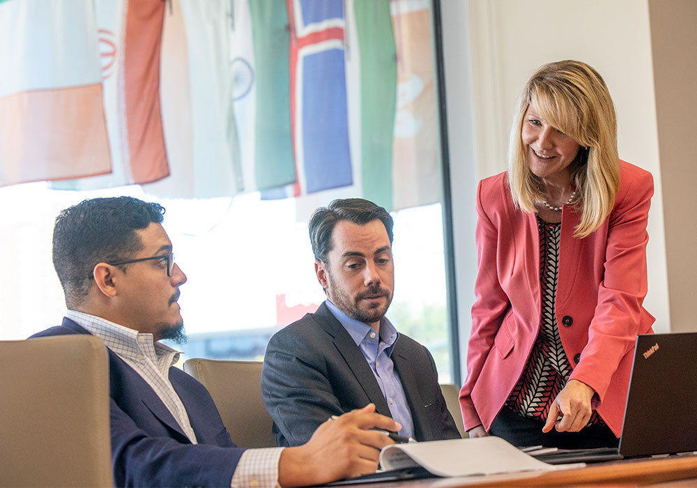 Professional dressed students sitting at a table talking with a professor.