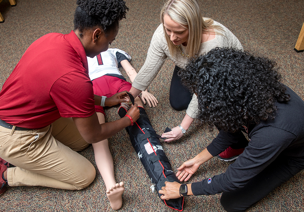Student in an athletic training class, splinting a leg of a mannequin.