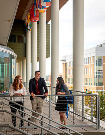 Three students standing at a railing of the Moore School.