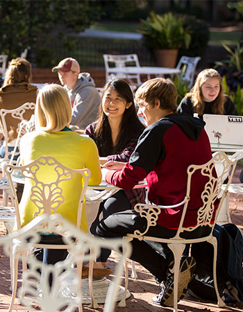 Clusters of students sit at various outdoor patio tables.