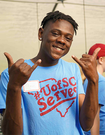 Student wearing a UofSC Serves t-shirt holding spurs up gesture and smiling at the camera.
