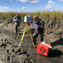 Two scientists in a creek at low tide with research equipment