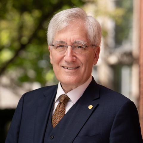 Headshot of a man with white hair wearing a suit standing outside