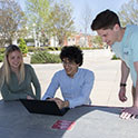 Three students looking at a computer at a table outside swearingen engineering center