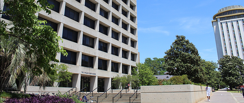 The Close-Hipp building, the home of the College of Hospitality, Retail and Sport Management during a clear sunny day. Close-Hipp is an 8-story building with an outdoor patio area surrounded by garden landscaping. The Capstone building, with a rotating restaurant at its top, is in the background.