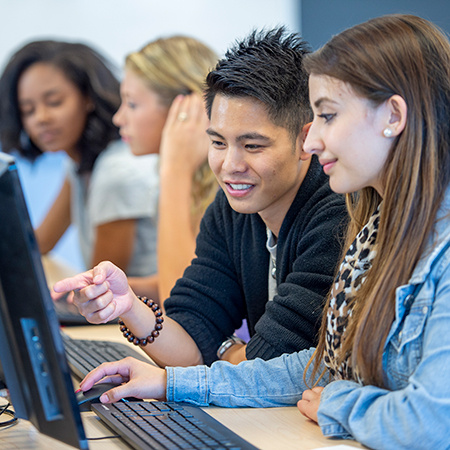 A small group of University students sit in a computer lab as they work on their assignments. They are each dressed casually and are seated in front of their individual computers.