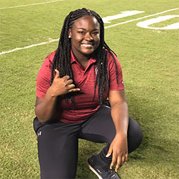 Lyric Swinton Lyric Swinton kneels on a football field and gives the "spurs up" hand signal