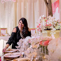 Nirjary Desai Nirjary Desai stands in a room decorated for a bridal reception with lush flowers and formal table setting
