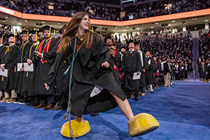 Alumni Sarah Sylvester wearing Cocky's feet while in graduation cap and down at the commencement ceremony.