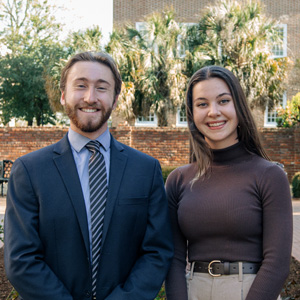 two people stand in a garden setting with a brick wall in the background