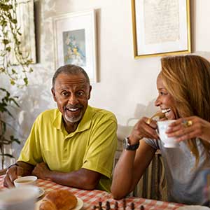 Older male drinks coffee at a table next to a younger female. 