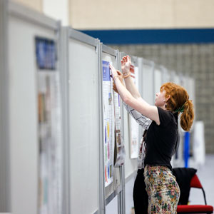 a woman tacks a poster to a bulletin board in a large convention hall