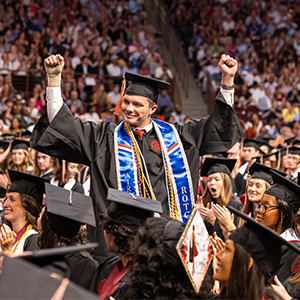 Student in cap and gown stands with fists in the air
