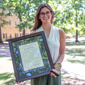 woman stands outside holding a framed award