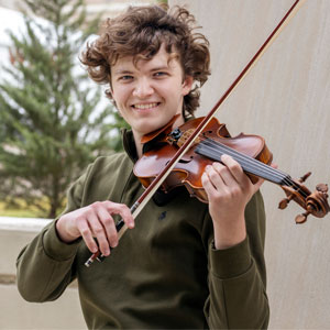 man stands outside a building holding a violin on his shoulder with the bow on the strings