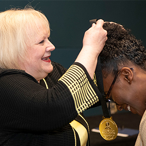 Ann Vail, dean of The Graduate School, puts an award around the neck of an award winner at the 2025 Recognition of Excellence Ceremony