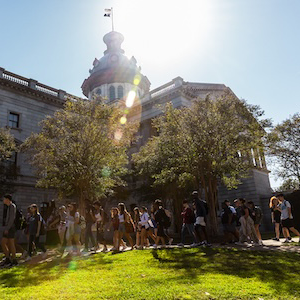 students walking by statehouse with sun shining over it