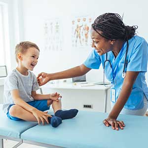Female nurse leans over exam table to check on male child. 