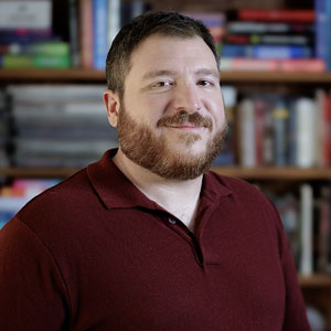 A headshot of script writer Patrick Pianezza in front of a bookshelf