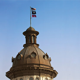 american flag, palmetto flag and USC flag flying above dome on statehouse