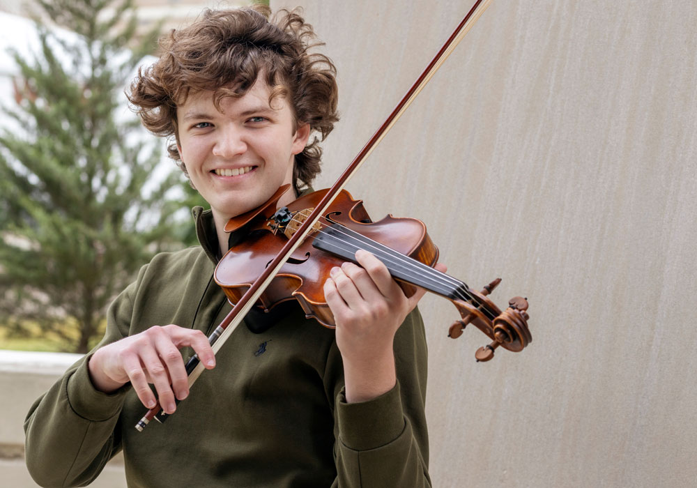 man plays the violin while standing in front of a building